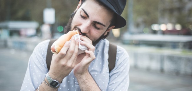 young handsome hipster gay modern man eating hot dog in town